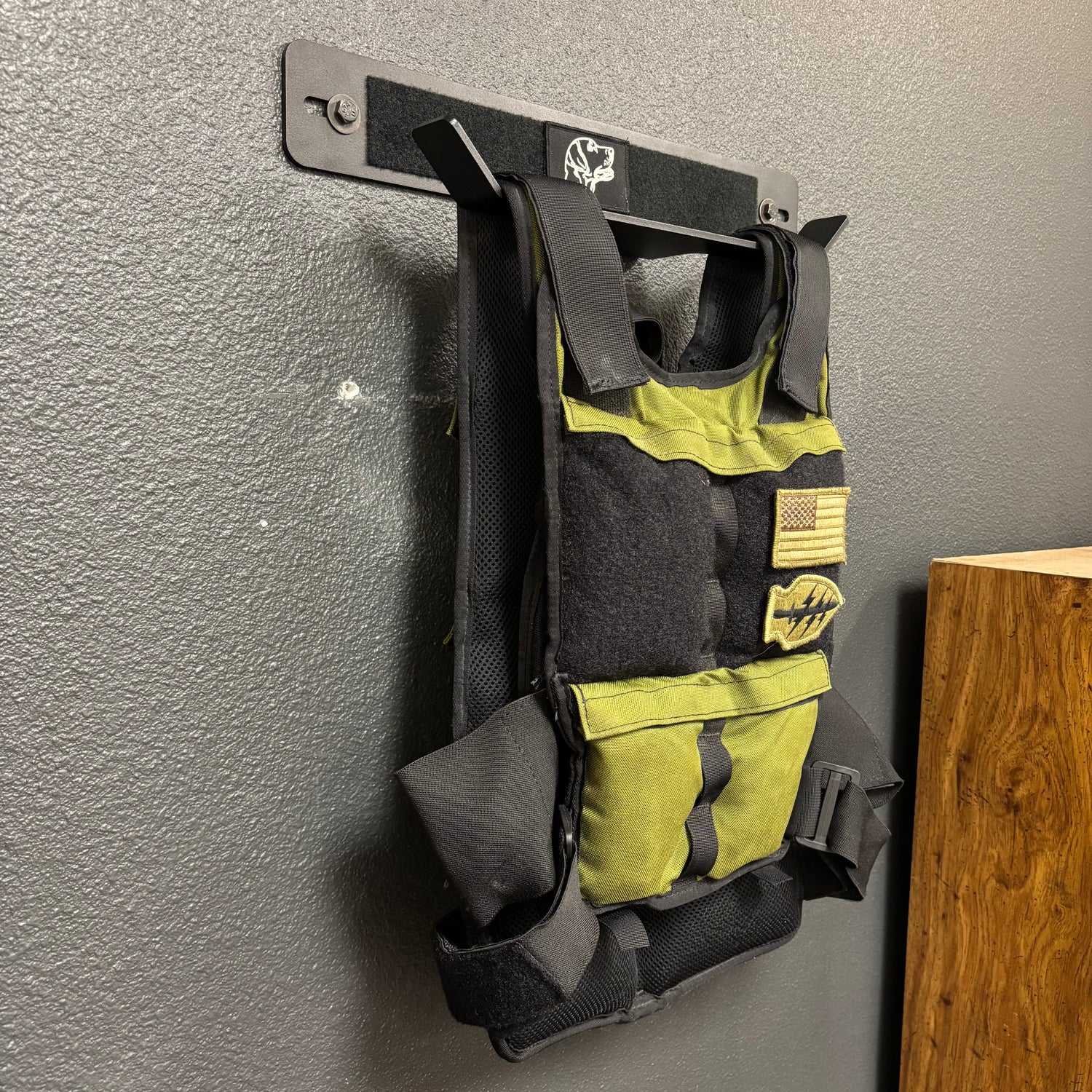 Black and green tactical vest hanging on a ruck storage product in a garage gym